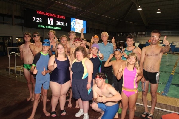  A large group of Special Olympians in bathing suits standing on the side of an indoor pool surrounding Harris Rosen, giving thumbs-ups. 