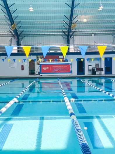 Looking down the lanes of an indoor swimming pool with blue and yellow flags hanging above the water.