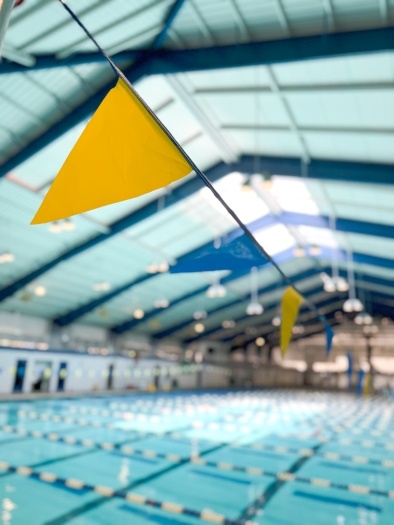 A close-up of a yellow flag on a string of blue and yellow flags hanging over an indoor pool at the Rosen Aquatic and Fitness Center. 