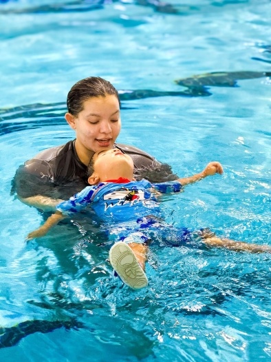 A female swim instructor guides a child on their back in a pool. 