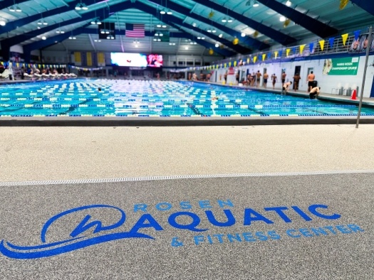 A close0p of the Rosen Aquatic and Fitness Center logo on the floor beside a large indoor swimming pool. 