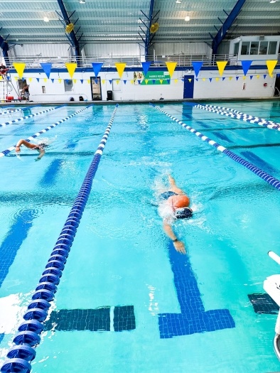  Swimmers swimming toward the camera in lanes of an indoor pool beneath blue and yellow flags at the RAFC.