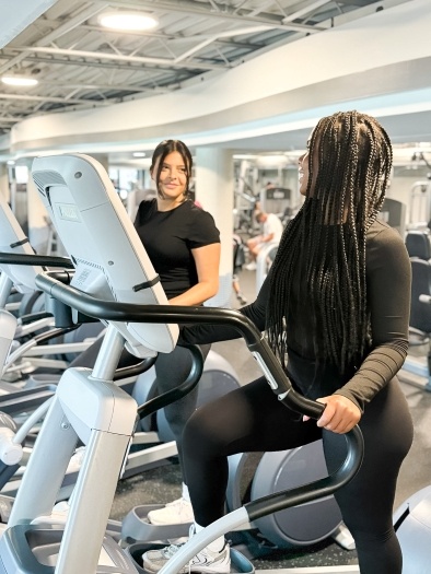 Two women in black mid-workout on elliptical machines in a well-lit fitness room at Rosen Aquatic & Fitness Center. 